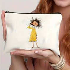 a woman holding up a white purse with a drawing of a girl in a yellow dress