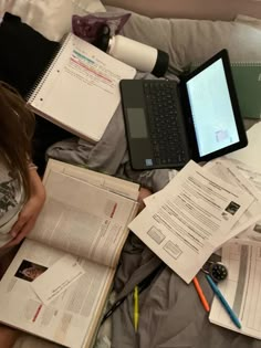 an open laptop computer sitting on top of a pile of papers next to a notebook