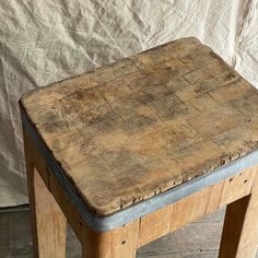 an old wooden table with metal legs on a wood floor next to a white sheet