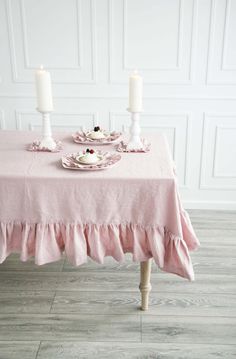 a table topped with two white candles and plates covered in pink ruffled linens