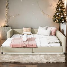 a bed with pillows and blankets on it next to a christmas tree in the corner