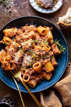 a blue plate topped with pasta and meat covered in sauce on top of a wooden table