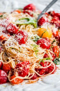 pasta with tomatoes, parmesan cheese and herbs on a white plate next to a fork