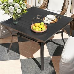 a bowl of fruit sitting on top of a wooden table next to chairs and flowers