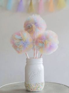 there are three colorful pom poms in a mason jar on the cake table