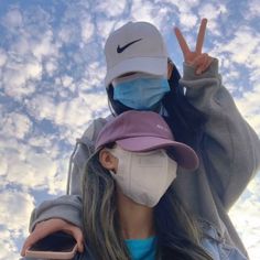 two people wearing face masks and one holding up the peace sign