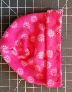 a pink hat with white snowflakes on it sitting on a cutting board next to a pair of scissors