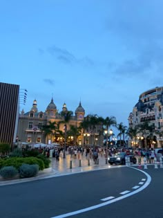 people are walking on the street in front of some buildings at dusk with palm trees