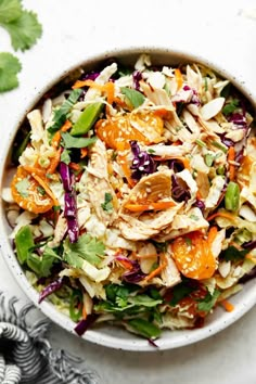 a white bowl filled with salad and topped with oranges, lettuce and chicken