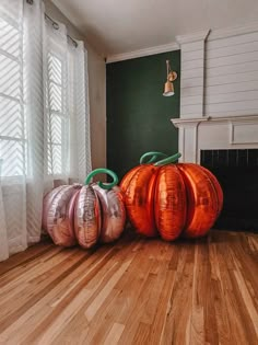 three shiny pumpkins sitting on the floor in front of a fire place and window