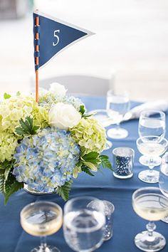 a blue table topped with a vase filled with white and blue flowers next to glasses