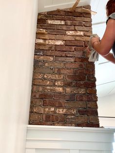 a woman is painting a brick wall with white paint on the top and bottom part