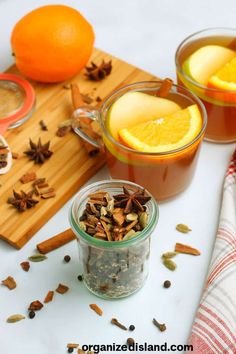 two jars filled with spices next to an orange slice and cinnamon on a cutting board