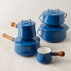 blue pots and pans with wooden handles on a white countertop next to each other