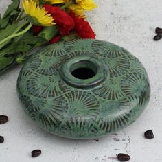 a green vase sitting on top of a table next to flowers and coffee beans in front of it