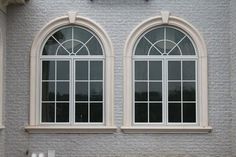 two windows on the side of a building with a clock mounted to it's face