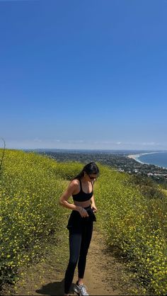 a woman standing on top of a dirt road next to a field filled with yellow flowers