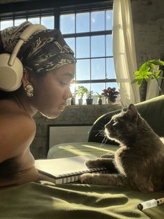 a woman with headphones on laying next to a cat