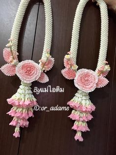 two pink and white necklaces with flowers hanging from the sides on a wooden surface