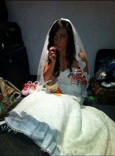 a woman in a wedding dress sitting on the floor next to luggage and holding a drink