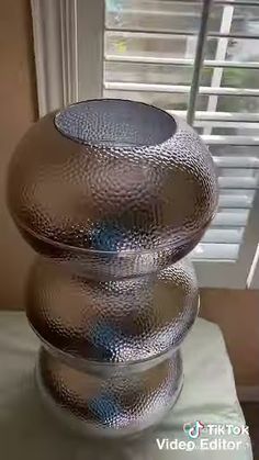 three silver vases sitting on top of a table next to a window with shutters