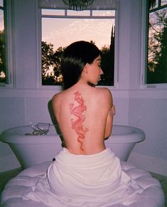 a woman with a dragon tattoo on her back sitting in front of a bathtub