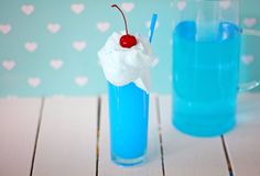 a blue drink with a cherry on top next to a cup filled with ice cream