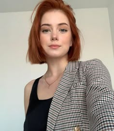 a woman with red hair wearing a jacket and black shirt is taking a selfie