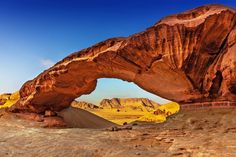 an arch shaped rock formation in the desert with mountains in the backgrouds