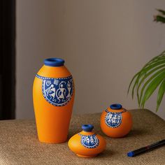 three orange vases sitting on top of a table next to a potted plant