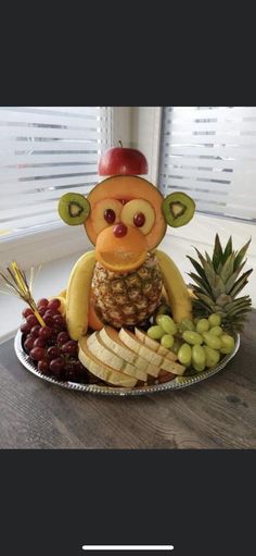 a monkey made out of fruit on top of a plate with grapes and pineapples