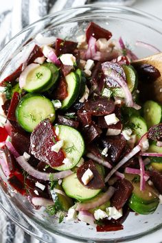 a glass bowl filled with cucumbers, onions and feta cheese on top of a table