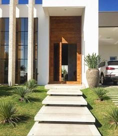 a modern house with grass and plants in the front yard, along with a car parked on the driveway