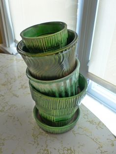 three green bowls are stacked on top of each other in front of a windowsill