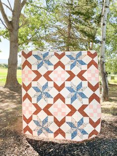 a quilt is hanging from a tree in the park with grass and trees behind it