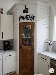 a kitchen with white cabinets and wooden door that says pantry on the wall above it