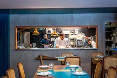 two men are cooking in a restaurant with blue walls and wooden chairs around the table