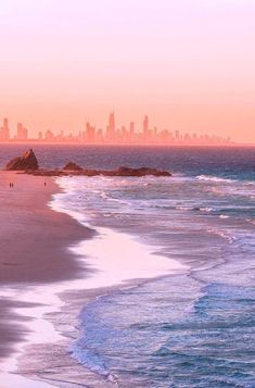 an ocean beach with people walking on it and the city skyline in the back ground