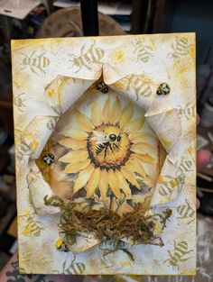 a person holding up a small card with a sunflower on it and bees in the center