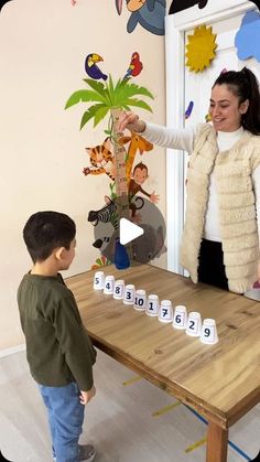 a woman standing next to a little boy at a table with letters on it and an animal wall decal behind her