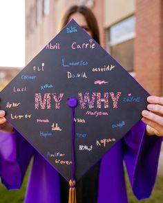 a woman in purple graduation gown holding up her cap with writing on it that says, my why?