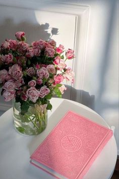 a vase with pink roses and a book on a table