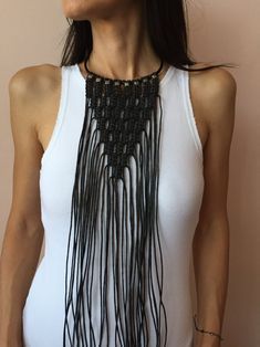 a woman wearing a white tank top with black beads on the neck and long necklace