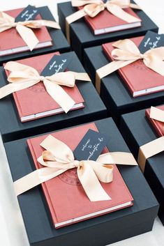 six black boxes with red and pink books tied with gold ribbons