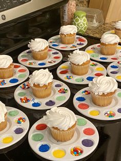 cupcakes with white frosting and sprinkles on plates in front of an oven