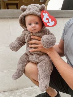 a man holding a baby wearing a teddy bear costume with a red tag on it's ear