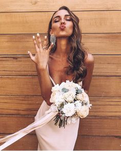 a woman in a white dress blowing bubbles with her hands and holding a flower bouquet