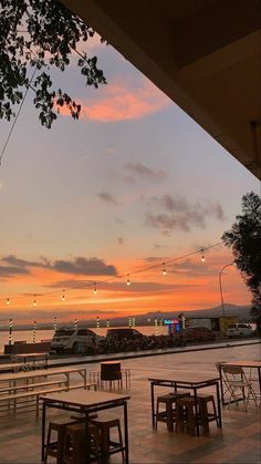 an empty patio with tables and chairs on it as the sun sets in the distance