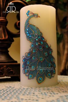 a white candle with a blue and green peacock on it's side sitting on a table