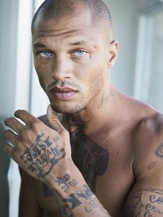 a shirtless man with tattoos on his arms and chest looking at the camera while standing in front of a window